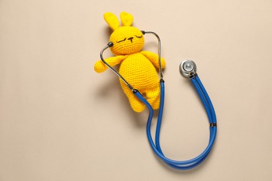 Photo of Pediatrics concept. Toy bunny with stethoscope on beige background, top view. Space for text