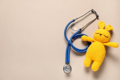 Photo of Pediatrics concept. Toy bunny with stethoscope on beige background, top view. Space for text