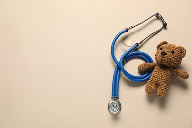 Photo of Pediatrics concept. Toy bear with stethoscope on beige background, top view. Space for text