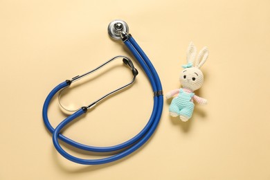 Photo of Pediatrics concept. Toy bunny with stethoscope on beige background, top view