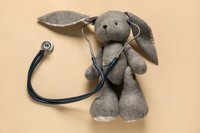 Photo of Pediatrics concept. Toy bunny with stethoscope on beige background, top view