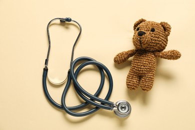 Photo of Pediatrics concept. Toy bear with stethoscope on beige background, top view