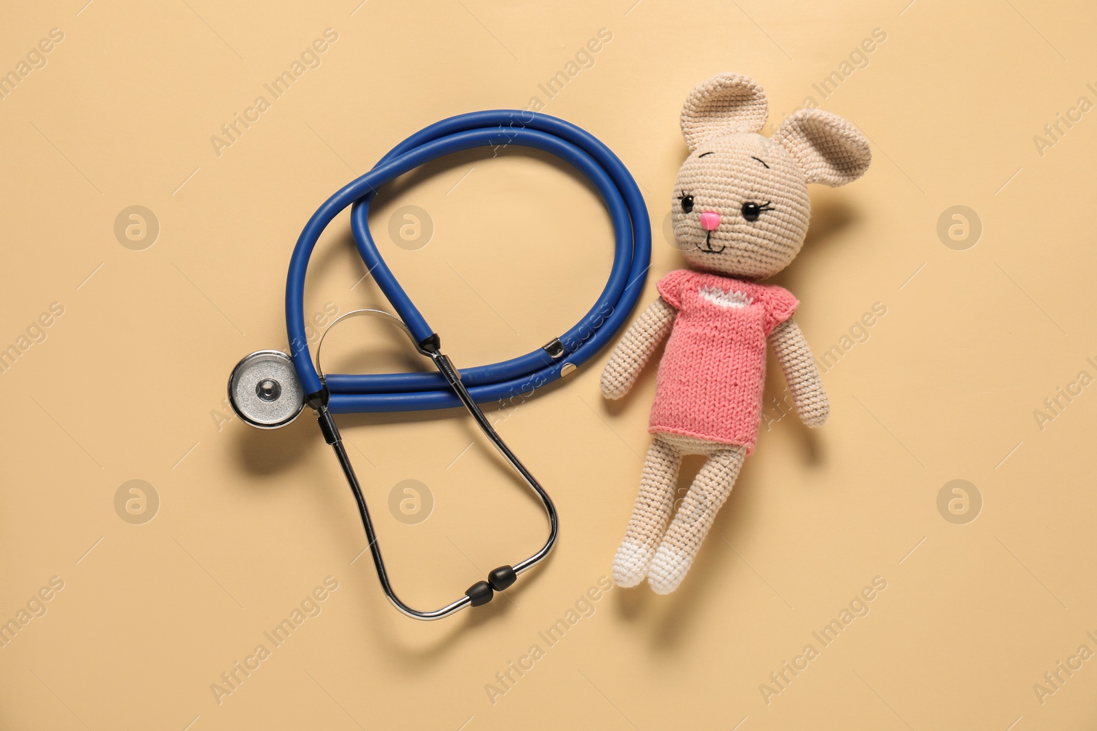 Photo of Pediatrics concept. Toy bunny with stethoscope on beige background, top view