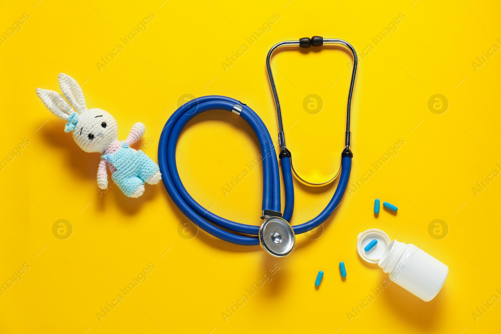 Photo of Pediatrics concept. Toy bunny with stethoscope and pills on yellow background, flat lay