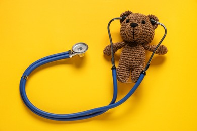 Photo of Pediatrics concept. Toy bear with stethoscope on yellow background, top view