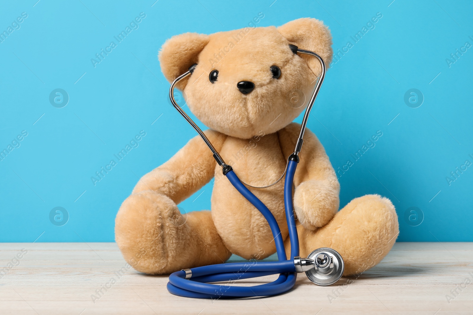 Photo of Pediatrics concept. Teddy bear with stethoscope on wooden table against light blue background