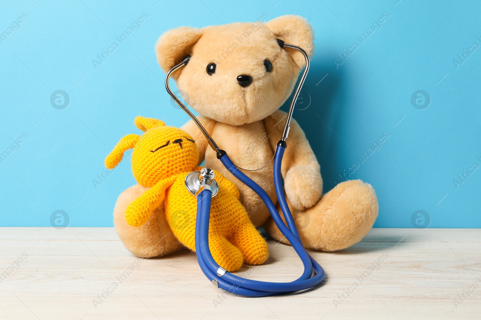 Photo of Pediatrics concept. Teddy bear and bunny toy with stethoscope on wooden table against light blue background