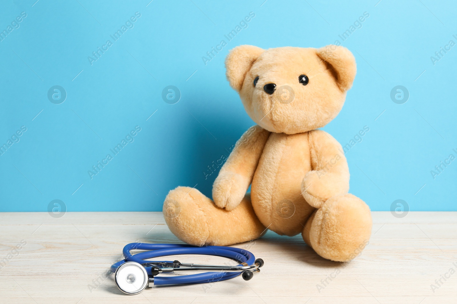 Photo of Pediatrics concept. Teddy bear with stethoscope on wooden table against light blue background