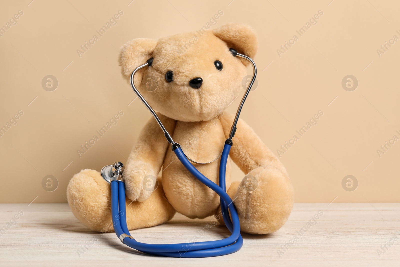 Photo of Pediatrics concept. Teddy bear with stethoscope on wooden table against beige background