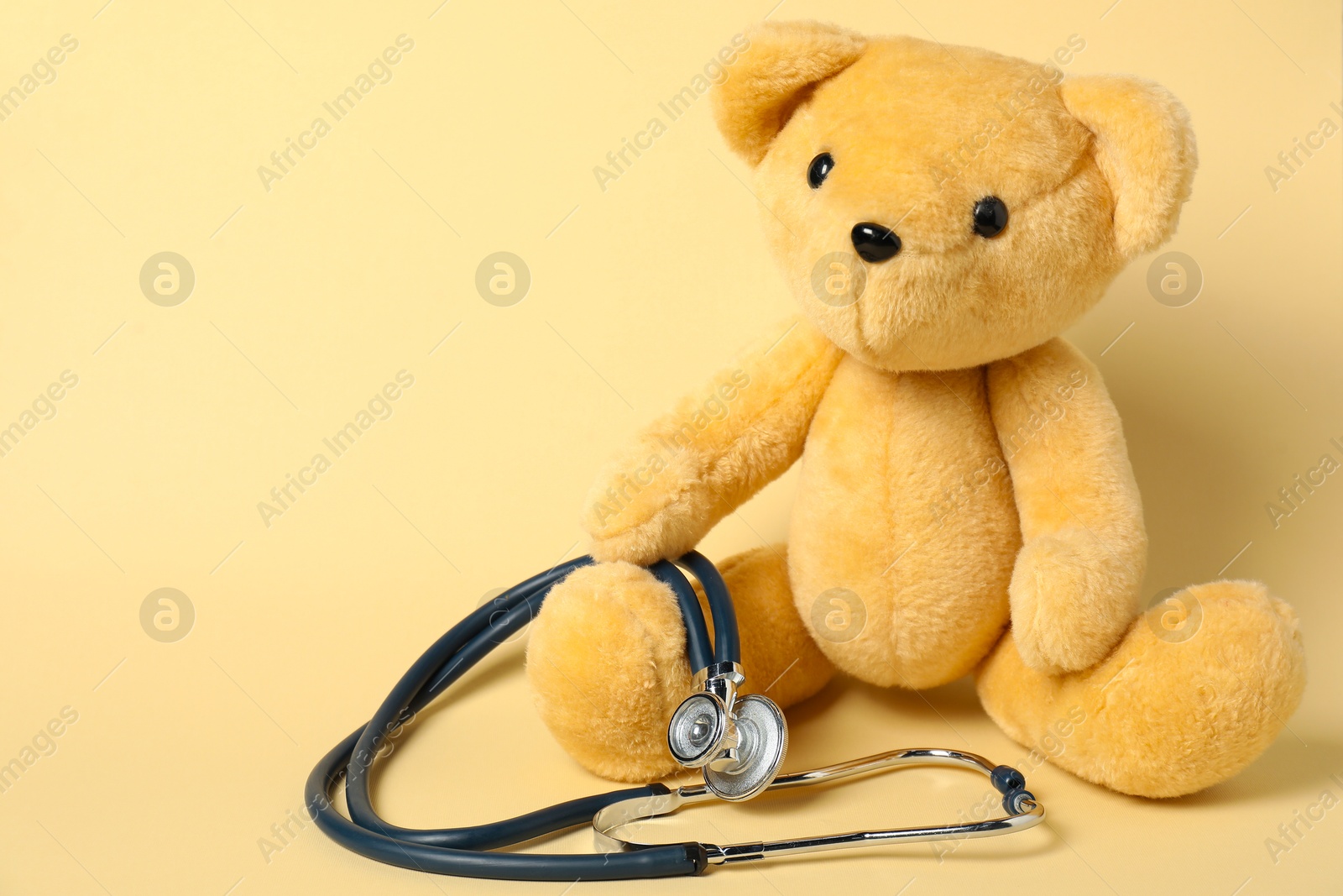 Photo of Pediatrics concept. Teddy bear with stethoscope on beige background, space for text