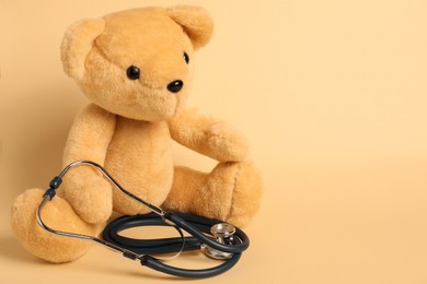 Photo of Pediatrics concept. Teddy bear with stethoscope on beige background, space for text