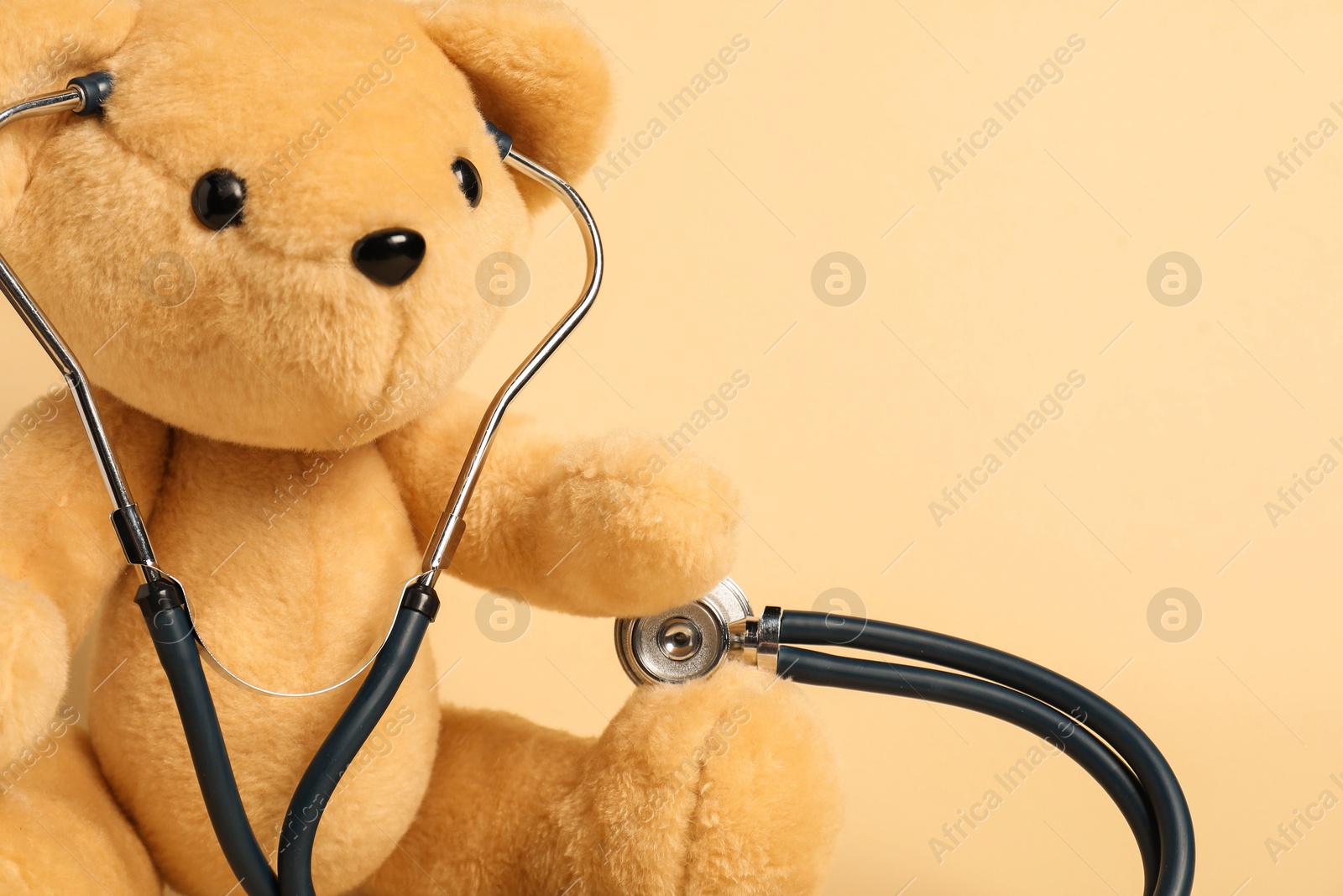 Photo of Pediatrics concept. Teddy bear with stethoscope on beige background, space for text