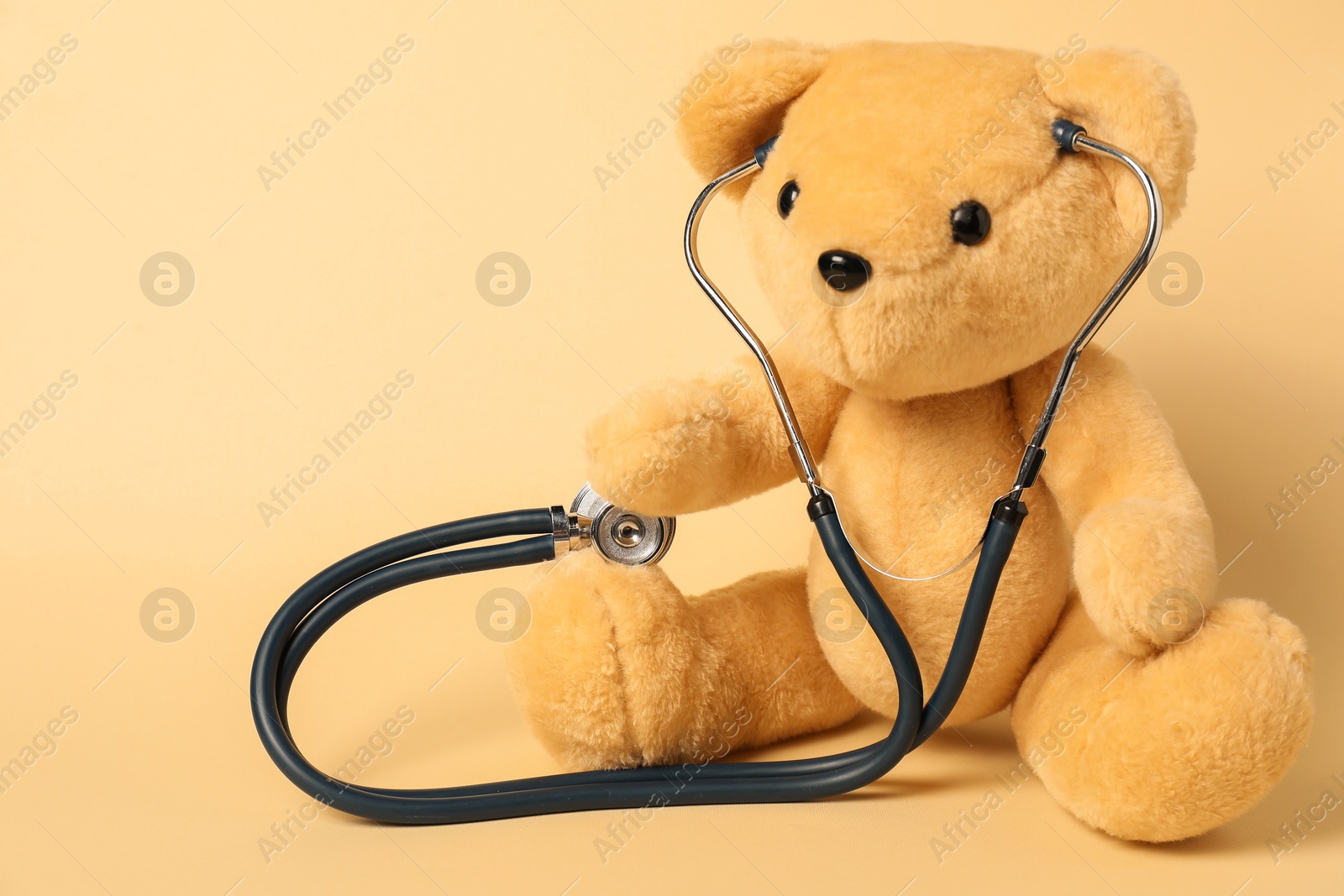 Photo of Pediatrics concept. Teddy bear with stethoscope on beige background, space for text