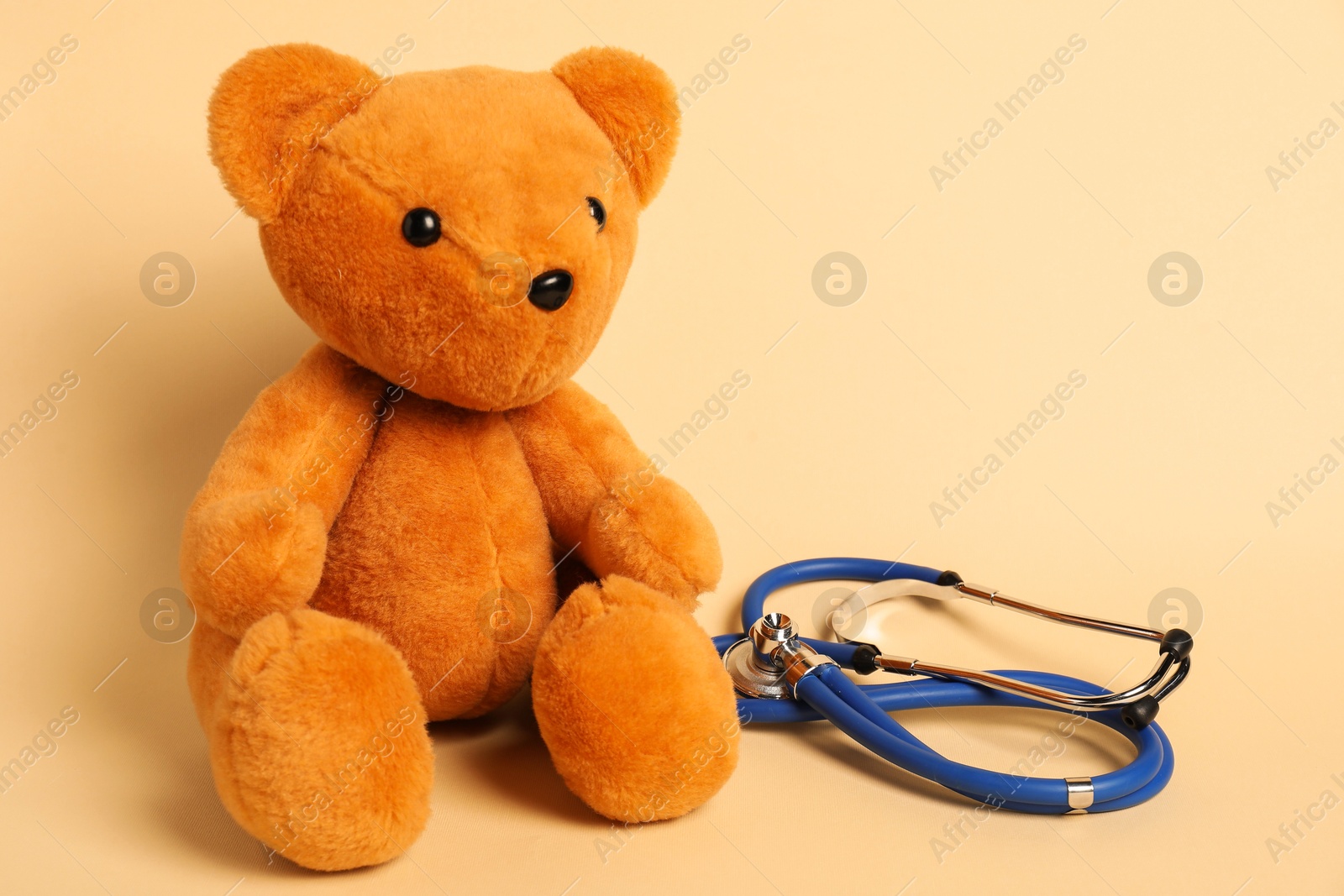 Photo of Pediatrics concept. Teddy bear with stethoscope on beige background, space for text