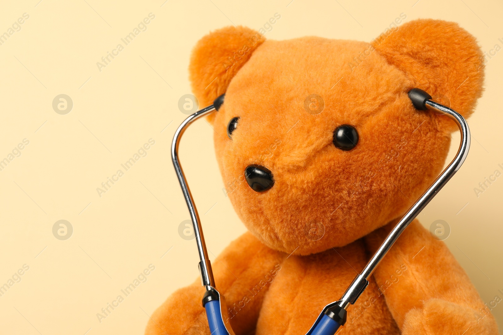 Photo of Pediatrics concept. Teddy bear with stethoscope on beige background, closeup