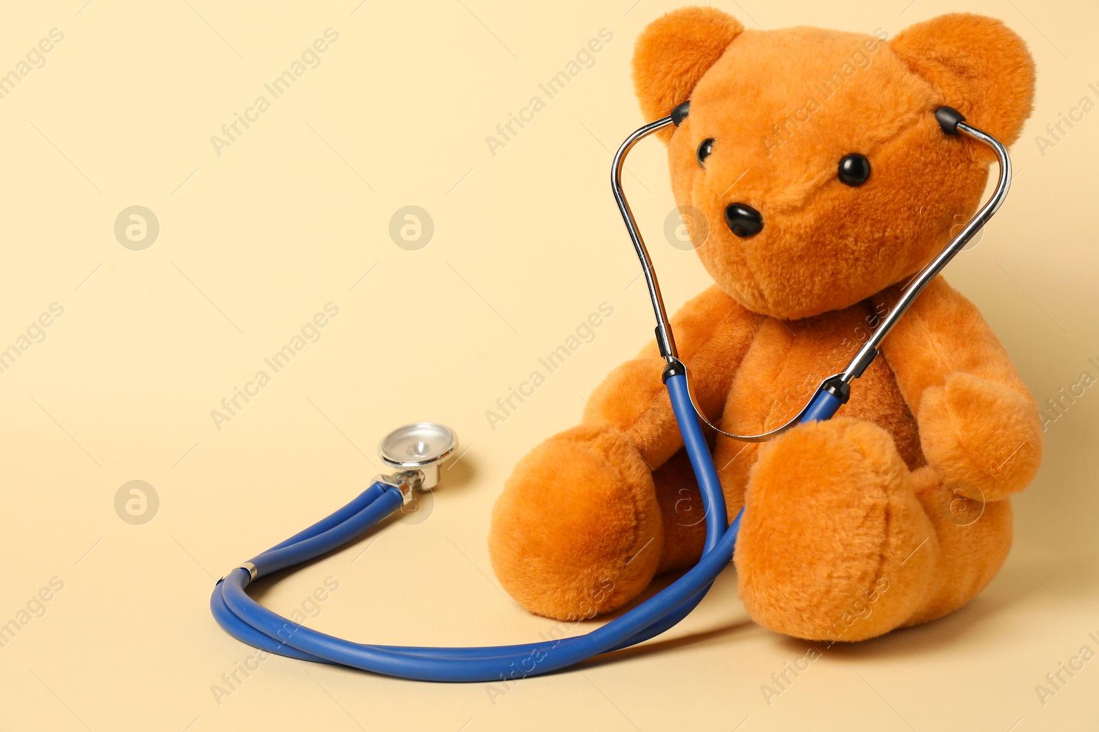 Photo of Pediatrics concept. Teddy bear with stethoscope on beige background, space for text