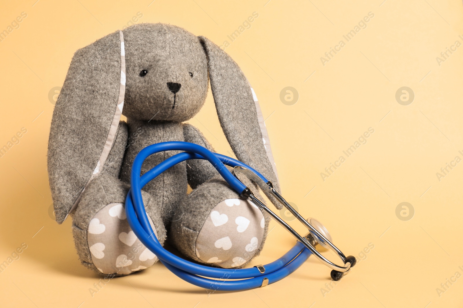 Photo of Pediatrics concept. Toy bunny with stethoscope on beige background, space for text