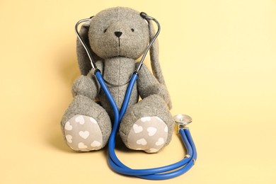 Photo of Pediatrics concept. Toy bunny with stethoscope on beige background, space for text