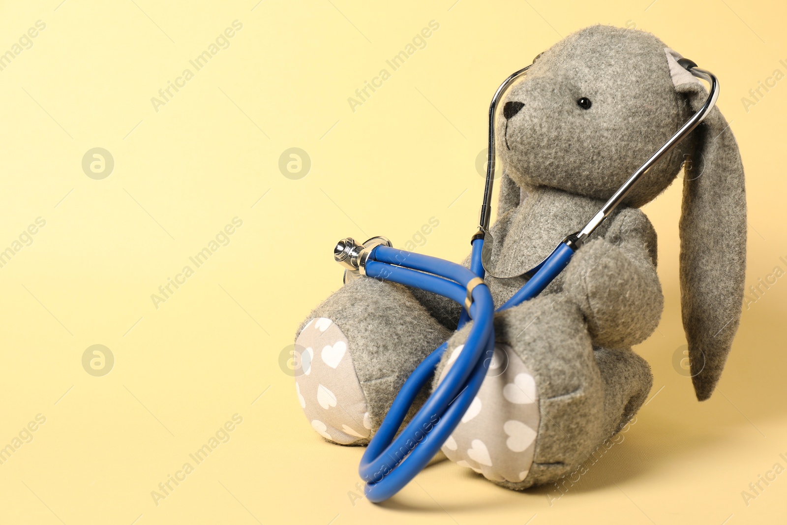 Photo of Pediatrics concept. Toy bunny with stethoscope on beige background, space for text