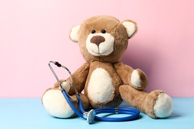 Photo of Pediatrics concept. Teddy bear with stethoscope on light blue wooden table against pink background