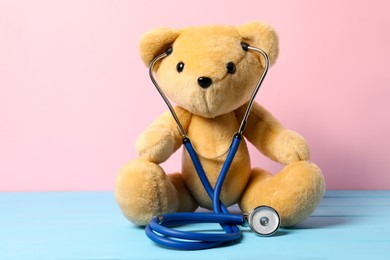 Photo of Pediatrics concept. Teddy bear with stethoscope on light blue wooden table against pink background