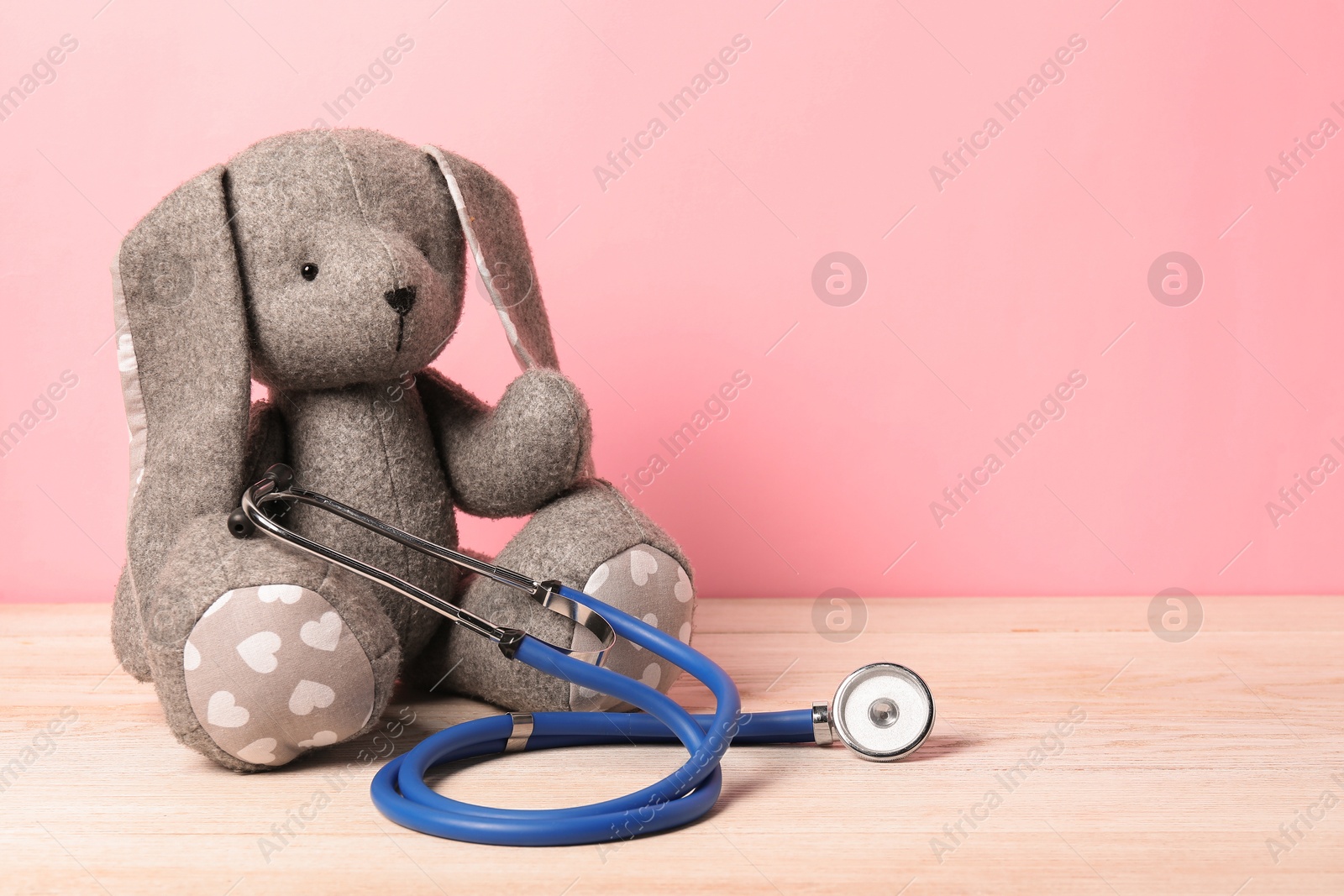 Photo of Pediatrics concept. Toy bunny with stethoscope on wooden table against pink background, space for text