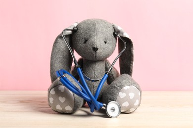 Photo of Pediatrics concept. Toy bunny with stethoscope on wooden table against pink background