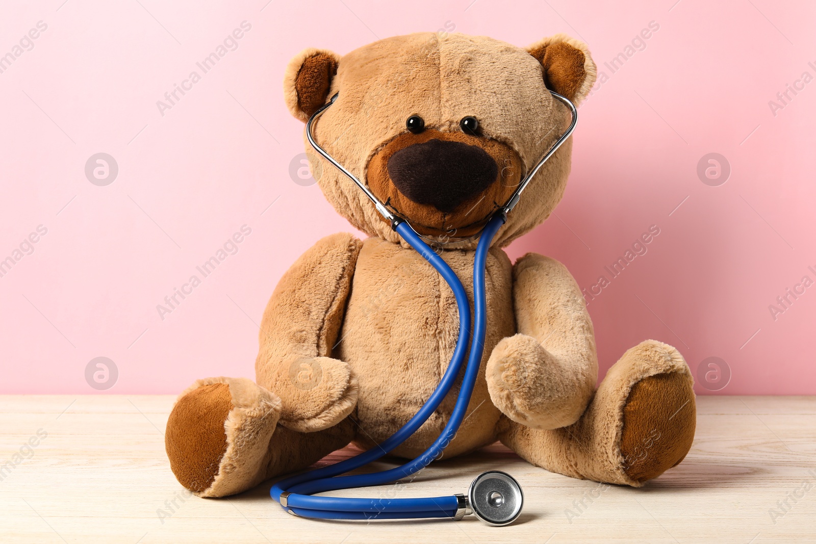 Photo of Pediatrics concept. Teddy bear with stethoscope on wooden table against pink background