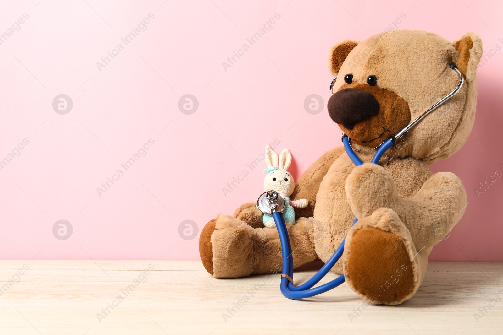 Photo of Pediatrics concept. Teddy bear and bunny toy with stethoscope on wooden table against pink background, space for text