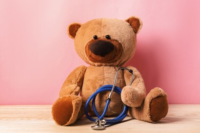 Photo of Pediatrics concept. Teddy bear with stethoscope on wooden table against pink background