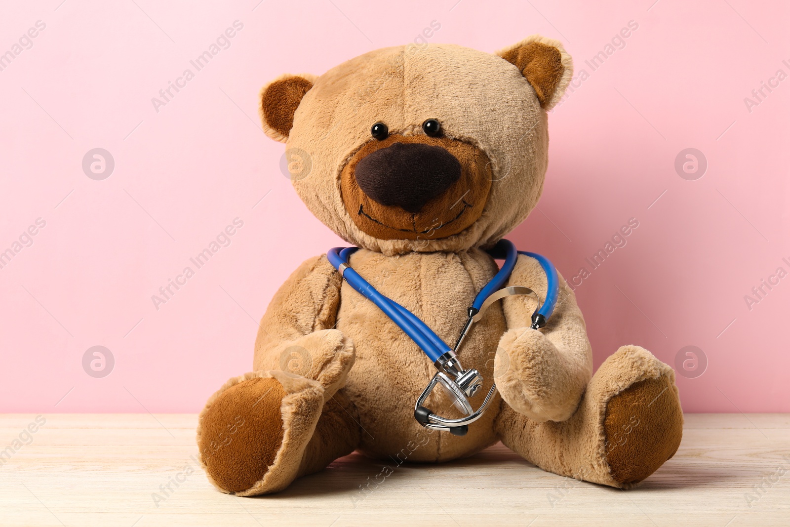 Photo of Pediatrics concept. Teddy bear with stethoscope on wooden table against pink background