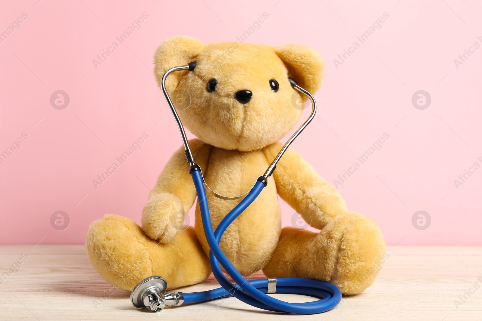 Photo of Pediatrics concept. Teddy bear with stethoscope on wooden table against pink background