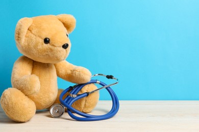 Photo of Pediatrics concept. Teddy bear with stethoscope on wooden table against light blue background, space for text