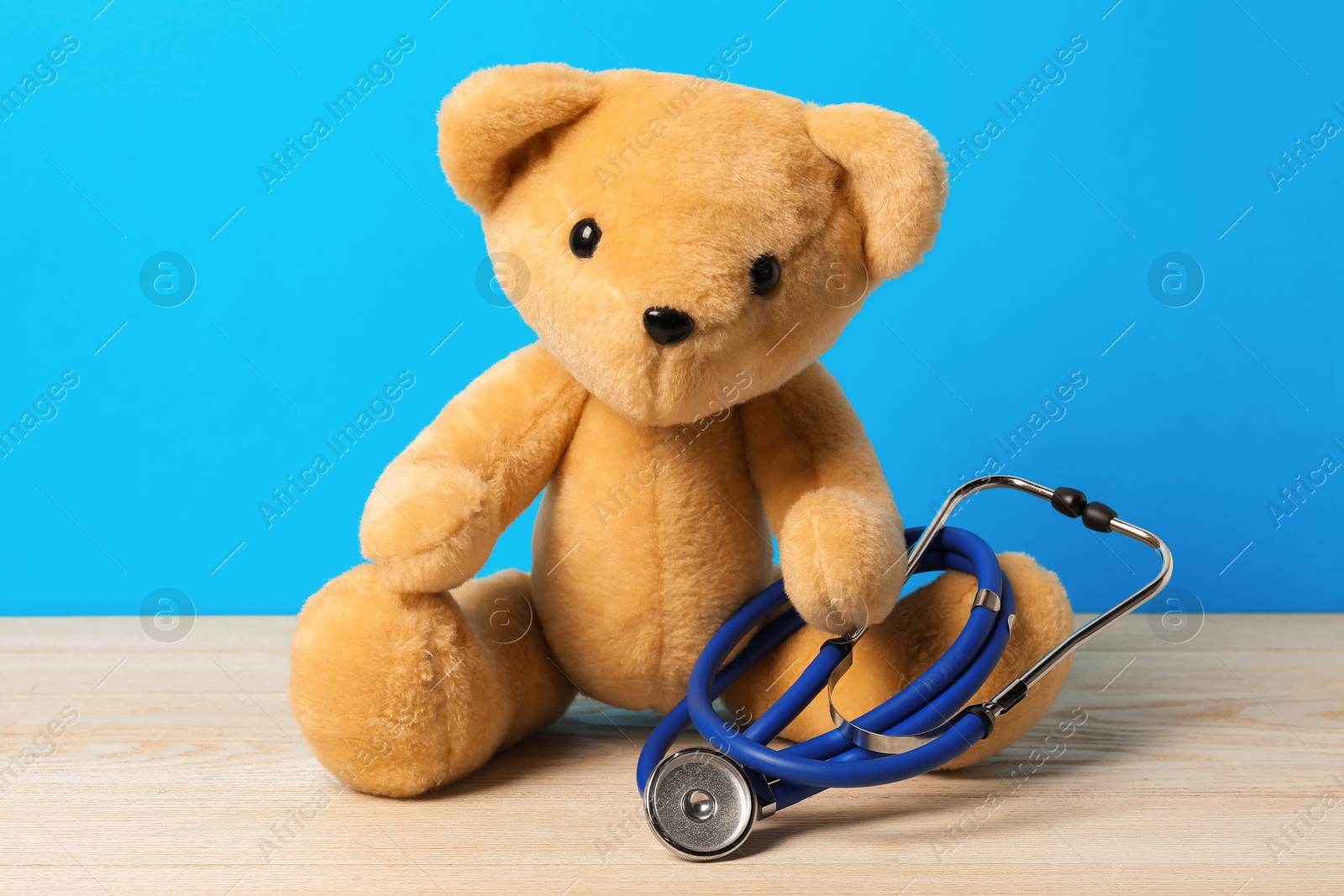 Photo of Pediatrics concept. Teddy bear with stethoscope on wooden table against light blue background