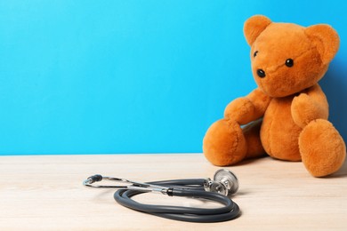 Photo of Pediatrics concept. Teddy bear with stethoscope on wooden table against light blue background, space for text