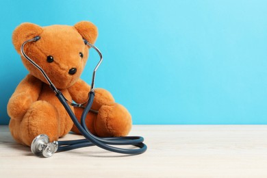 Photo of Pediatrics concept. Teddy bear with stethoscope on wooden table against light blue background, space for text