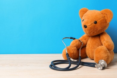 Photo of Pediatrics concept. Teddy bear with stethoscope on wooden table against light blue background, space for text