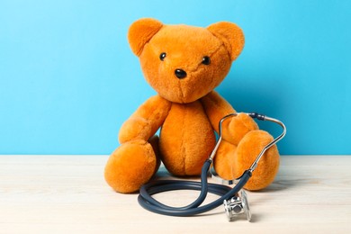 Photo of Pediatrics concept. Teddy bear with stethoscope on wooden table against light blue background