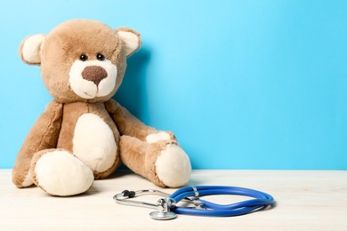 Photo of Pediatrics concept. Teddy bear with stethoscope on wooden table against light blue background, space for text