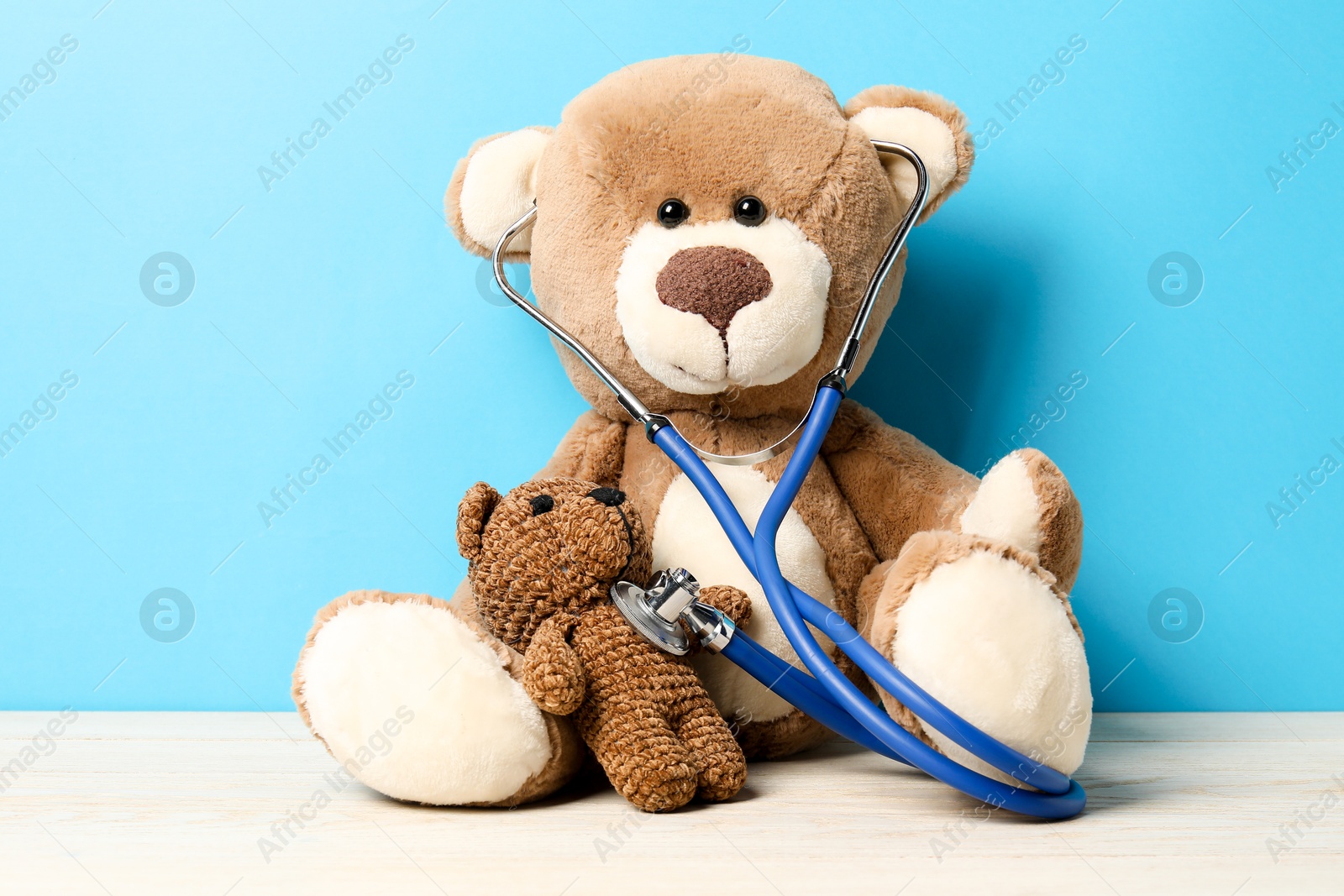 Photo of Pediatrics concept. Toy bears with stethoscope on wooden table against light blue background