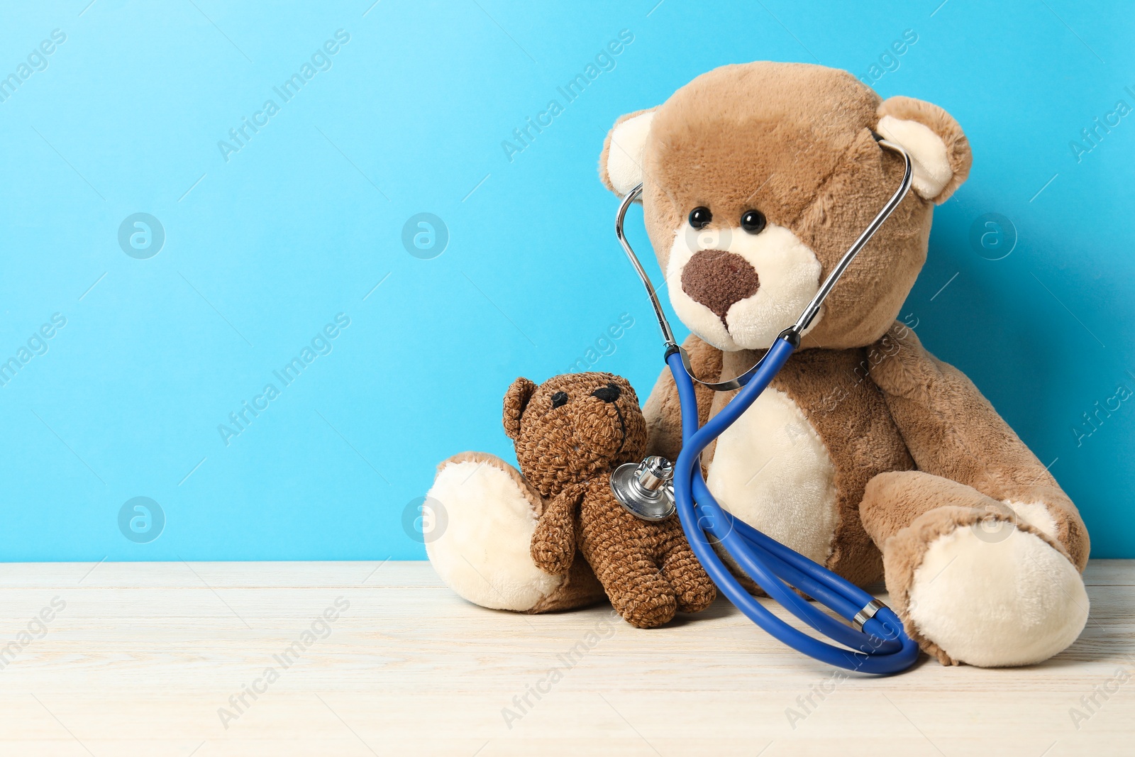 Photo of Pediatrics concept. Toy bears with stethoscope on wooden table against light blue background, space for text