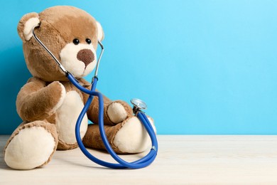 Photo of Pediatrics concept. Teddy bear with stethoscope on wooden table against light blue background, space for text