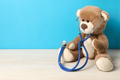 Photo of Pediatrics concept. Teddy bear with stethoscope on wooden table against light blue background, space for text