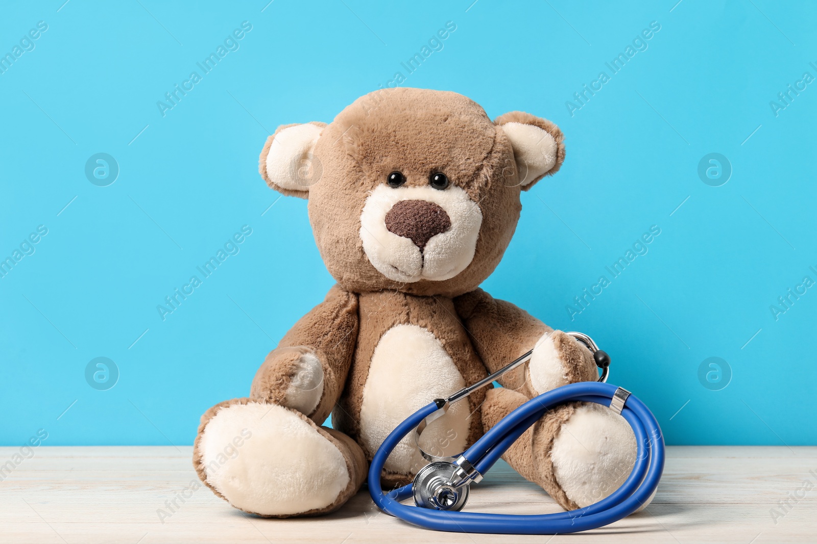 Photo of Pediatrics concept. Teddy bear with stethoscope on wooden table against light blue background