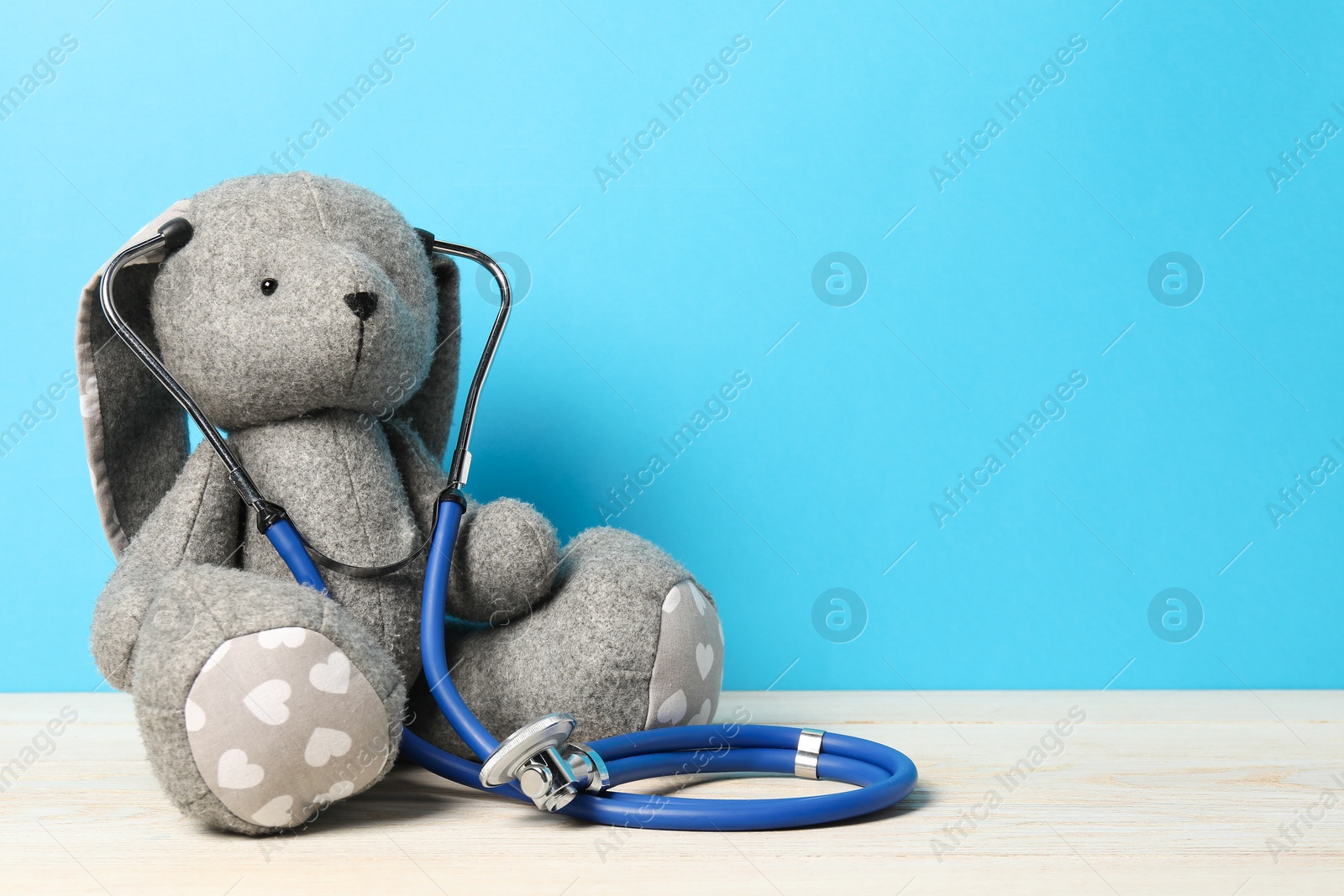 Photo of Pediatrics concept. Toy bunny with stethoscope on wooden table against light blue background, space for text