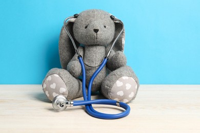 Photo of Pediatrics concept. Toy bunny with stethoscope on wooden table against light blue background