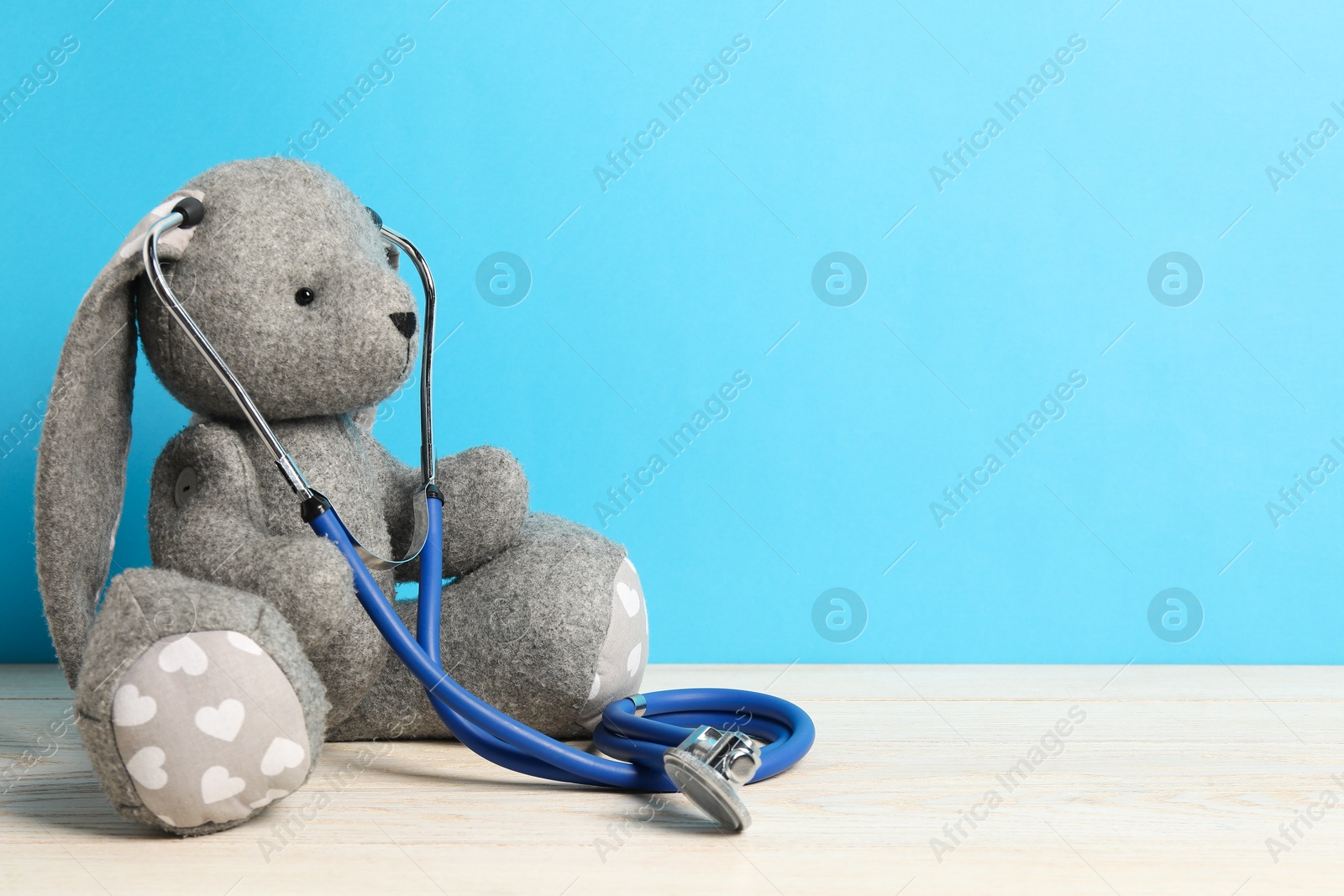 Photo of Pediatrics concept. Toy bunny with stethoscope on wooden table against light blue background, space for text