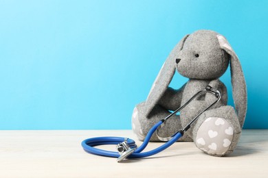 Photo of Pediatrics concept. Toy bunny with stethoscope on wooden table against light blue background, space for text