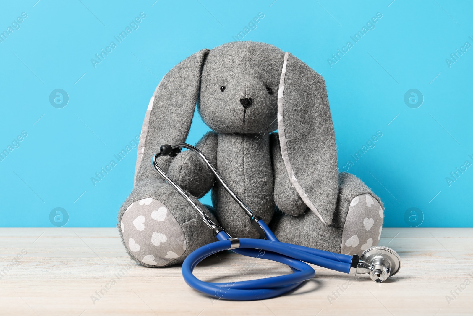 Photo of Pediatrics concept. Toy bunny with stethoscope on wooden table against light blue background