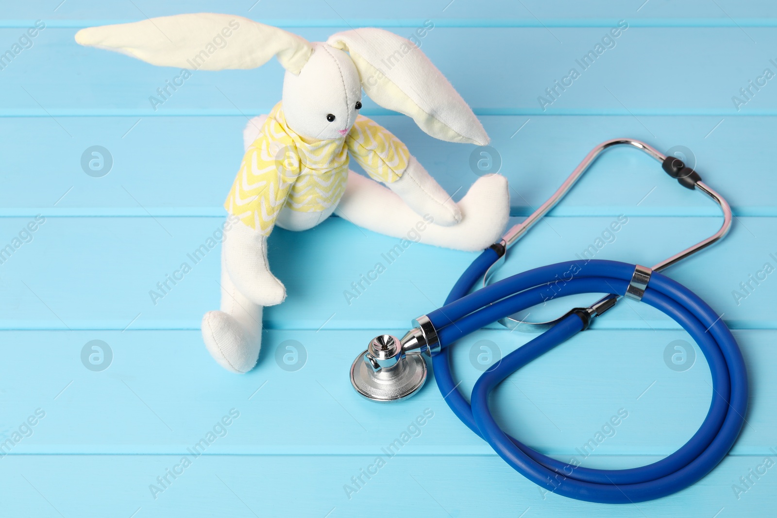 Photo of Pediatrics concept. Toy bunny and stethoscope on light blue wooden table